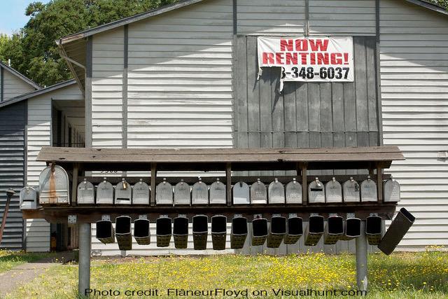 A building with multiple mailboxes and a 'for rent' sign