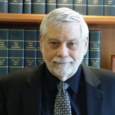 Edwin, black suit, silver tie, in front of a bookshelf